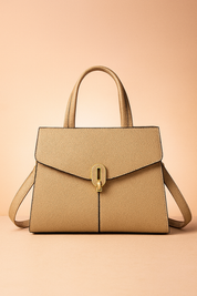 Structured beige leather handbag with gold turn-lock clasp, black edge piping, top handles, and shoulder strap, set on a studio platform.