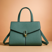 Structured teal handbag with pebbled texture, gold oval clasp, and dual handles, styled on a neutral table with soft gradient background.