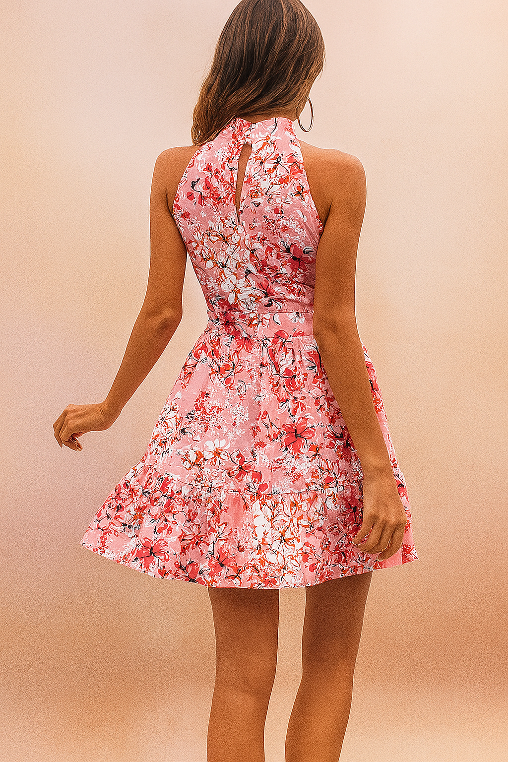 A model wearing the Carlotta sheer summer dress in pink with a halter neck, styled for the Summer Edition. The dress features a vibrant floral print, sleeveless cut, and a flattering waist tie, perfect for sunny days.