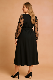 Back view of a black plus size midi dress with floral sheer sleeves, modeled by a woman with long ash blonde hair, perfect for elegant evening occasions.