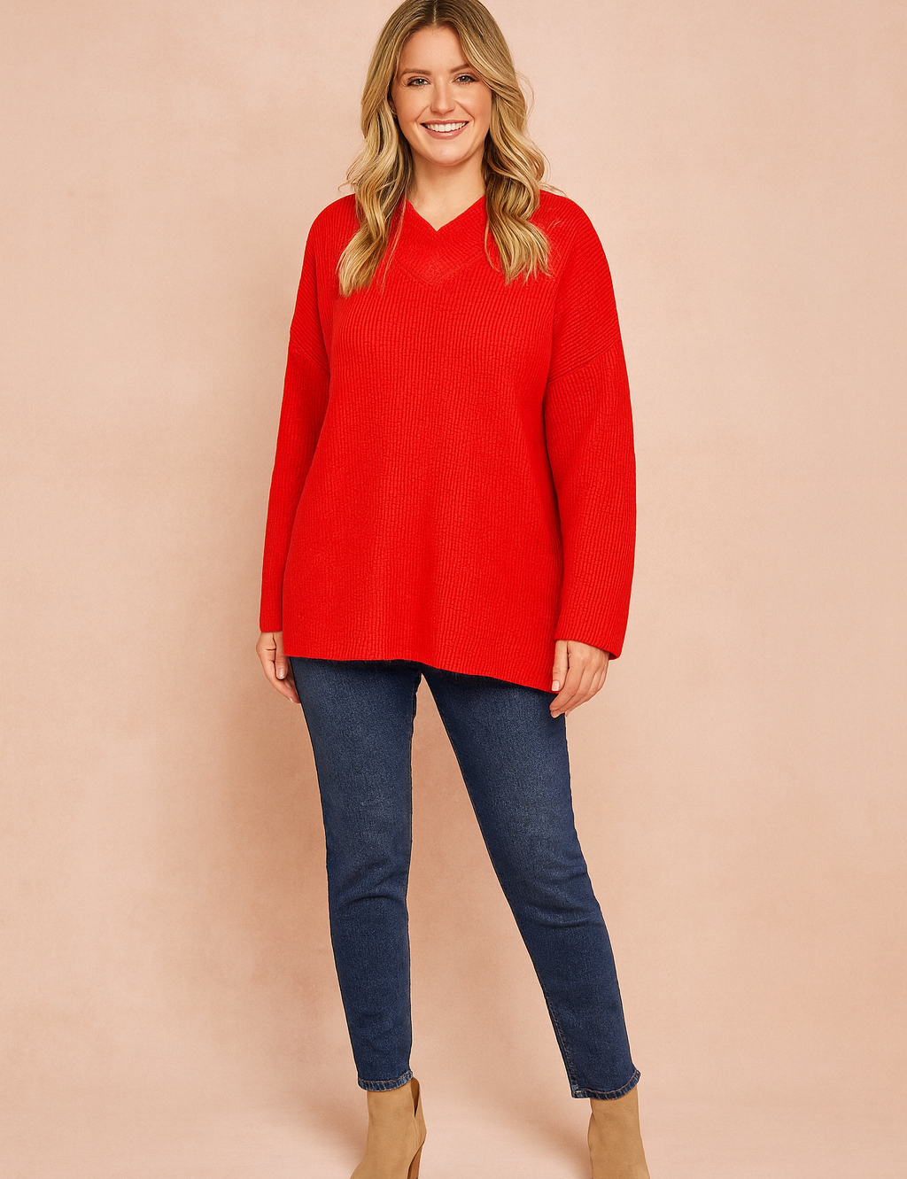 Bright red oversized knit sweater with V-neckline and long sleeves, paired with dark blue skinny jeans and beige suede ankle boots.