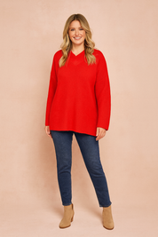 Bright red oversized knit sweater with V-neckline and long sleeves, paired with dark blue skinny jeans and beige suede ankle boots.