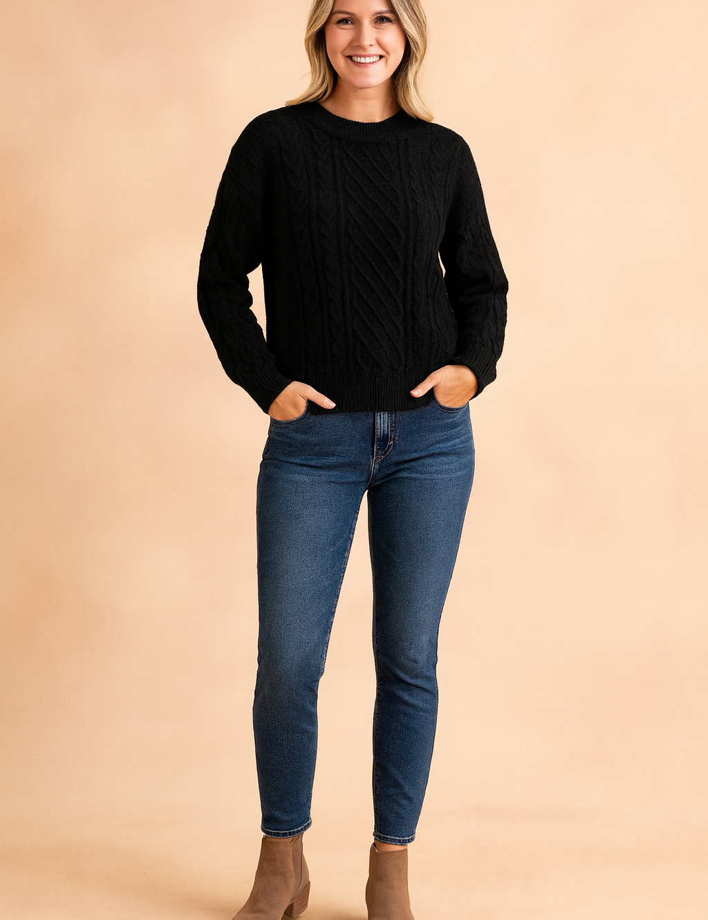 Black cable knit crew neck sweater with ribbed cuffs and hem, paired with dark-wash skinny jeans and taupe suede ankle boots.