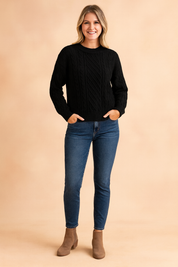 Black cable knit crew neck sweater with ribbed cuffs and hem, paired with dark-wash skinny jeans and taupe suede ankle boots.