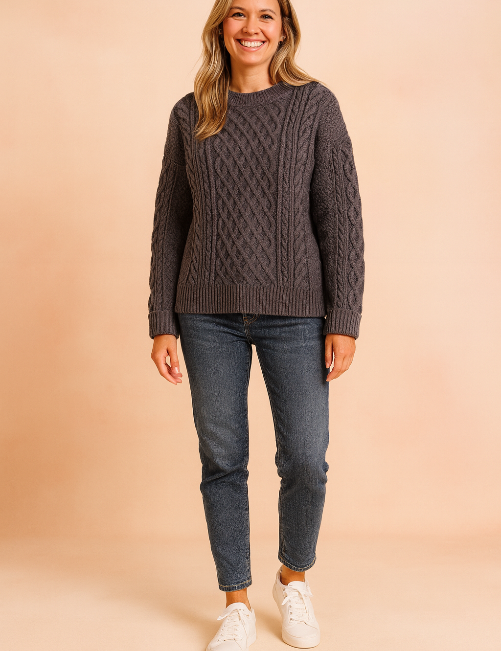 Dark gray cable-knit sweater with diamond and braid patterns, paired with medium-wash straight-leg jeans and white sneakers.