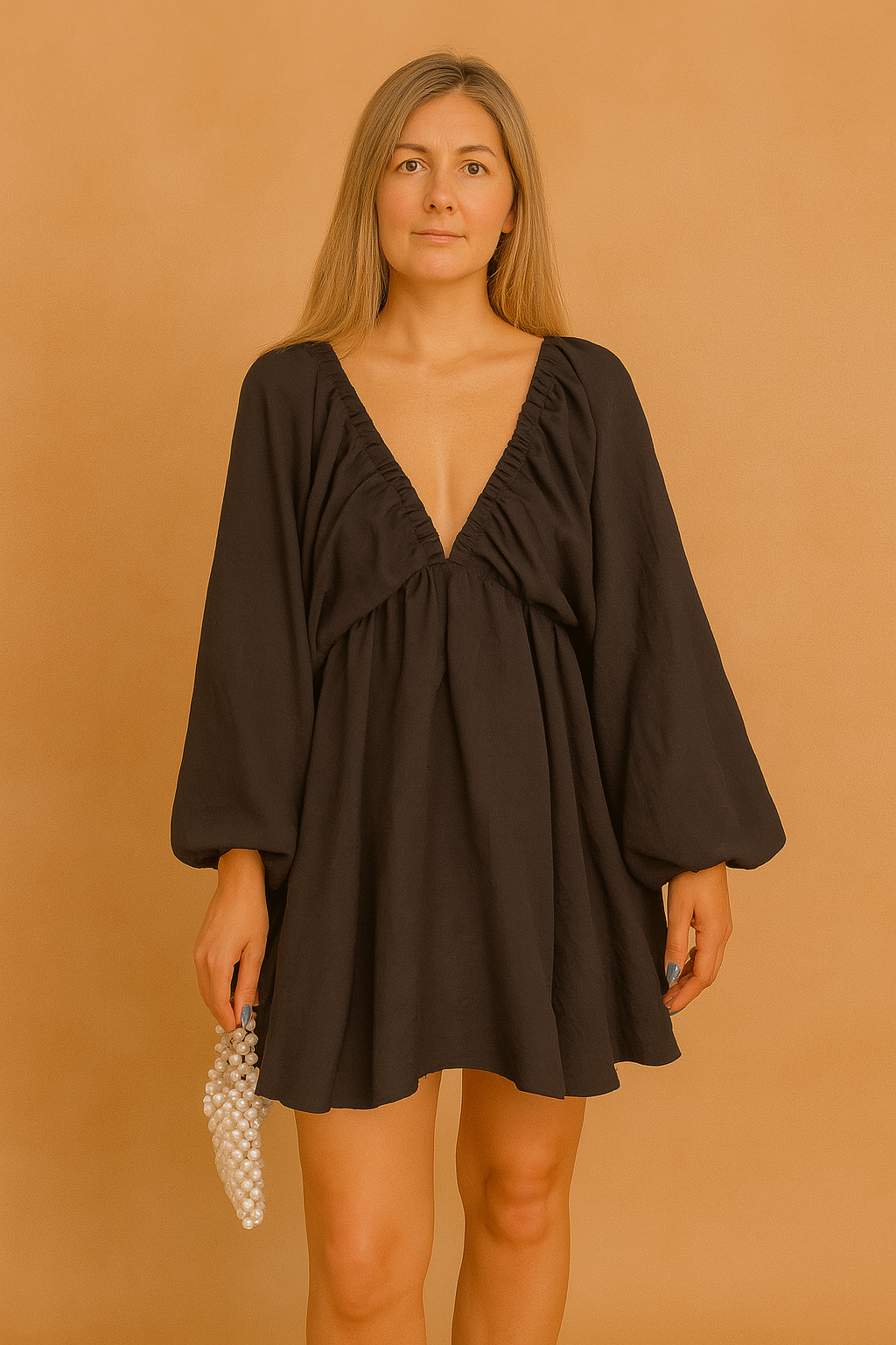 A black mini dress with bishop sleeves, posing against a soft sand and pastel pink background in a fashion shoot style.