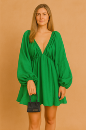 A green mini dress with bishop sleeves, posing against a soft sand and pastel pink background in a fashion shoot style.