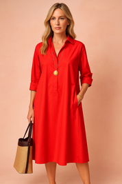 Elegancka, dojrzała kobieta w czarnej, minimalistycznej sukience koszulowej o luźnym kroju z kieszeniami, wystylizowana na swobodną elegancję w miejskim otoczeniu.