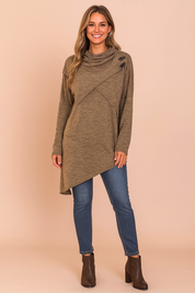 Asymmetrical heathered brown sweater with high cowl neckline, diagonal seam detailing, and three black button accents at the shoulder, paired with slim-fit blue denim jeans and dark brown ankle boots.