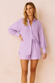 Lavender two-piece women's summer set featuring a long-sleeve, textured button-down shirt with voluminous sleeves and matching relaxed-fit high-waisted shorts. Made from lightweight breathable fabric, perfect for casual chic resort wear or daytime styling.