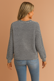 Black and white textured knit sweater with horizontal stripes, crew neckline, and relaxed fit paired with mid-rise light wash skinny jeans, accessorized with a tan suede clutch.