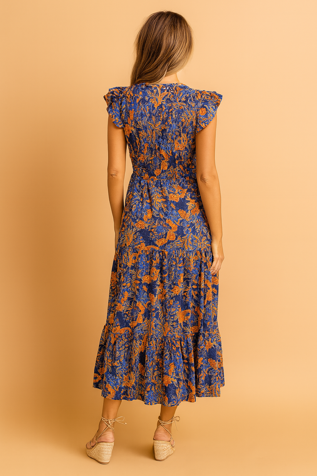 Back view of a navy blue and orange floral print midi dress with flutter sleeves, smocked bodice, defined waist, and a tiered hemline, featuring a lightweight flowy fabric with a vivid vintage-inspired botanical pattern.