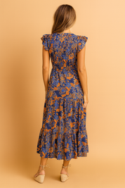 Back view of a navy blue and orange floral print midi dress with flutter sleeves, smocked bodice, defined waist, and a tiered hemline, featuring a lightweight flowy fabric with a vivid vintage-inspired botanical pattern.