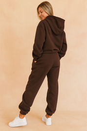 Back view of a dark brown hoodie and jogger co-ord set with elasticated cuffs and relaxed seams, styled for a clean and sporty silhouette paired with white sneakers.