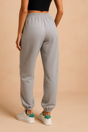 Back view of heather gray jogger sweatpants with elastic waistband and cuffed ankles, styled with green-accented white sneakers for a casual streetwear outfit.