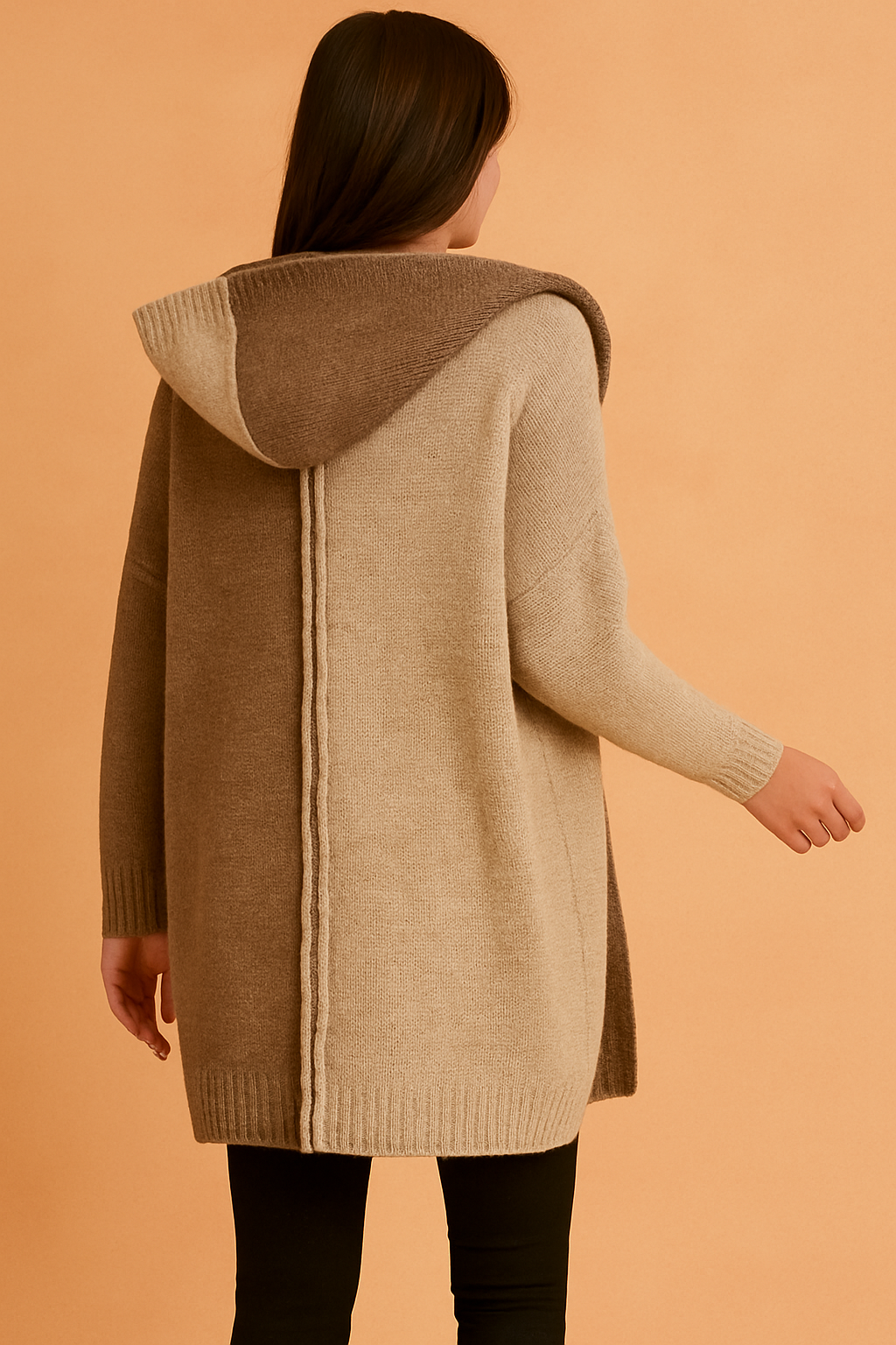 Back view of a two-tone knit hooded cardigan in light beige and medium brown, featuring a vertical seam detail, paired with black leggings.