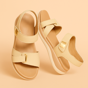 Beige double-strap sandals with gold-toned buckles and cushioned tan insoles, featuring a slightly raised white sole and a smooth synthetic leather finish