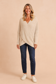 Beige crossover knit sweater with long sleeves, paired with dark blue straight-leg jeans and white sneakers.