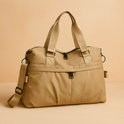 Beige nylon duffel-style tote bag with dual top handles, black zipper accents, pleated front pocket, and adjustable shoulder strap in matching color.