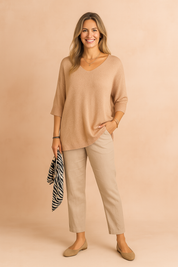 Lightweight loose-fit knit blouse in a soft peach-beige tone, featuring a V-neckline and elbow-length sleeves, styled with casual light beige trousers.