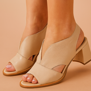 Beige open-toe block heel sandals crafted from soft-grain leather with curved asymmetrical cutouts, wide front strap, and slingback design for a modern, sculpted silhouette.