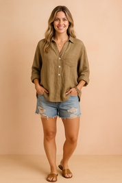 Oversized linen shirt in warm beige with a V-neck and three front white buttons, featuring a chest pocket and paired with distressed light blue denim shorts with heavy fraying.