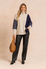 Beige and navy colorblock knit turtleneck sweater with ribbed hem and cuffs, paired with black leather-look trousers and black ankle boots for a chic winter outfit.