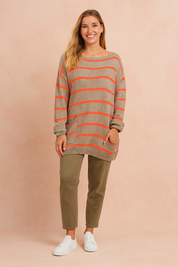 Beige oversized knit sweater with horizontal orange stripes, featuring a front pocket and rolled sleeves, paired with olive-green straight-leg pants and white low-top sneakers.