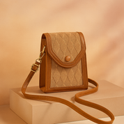 Beige quilted crossbody bag with diamond stitching, brown faux leather trim, rounded flap closure, and gold-toned hardware, displayed on a neutral sand and peach gradient background.
