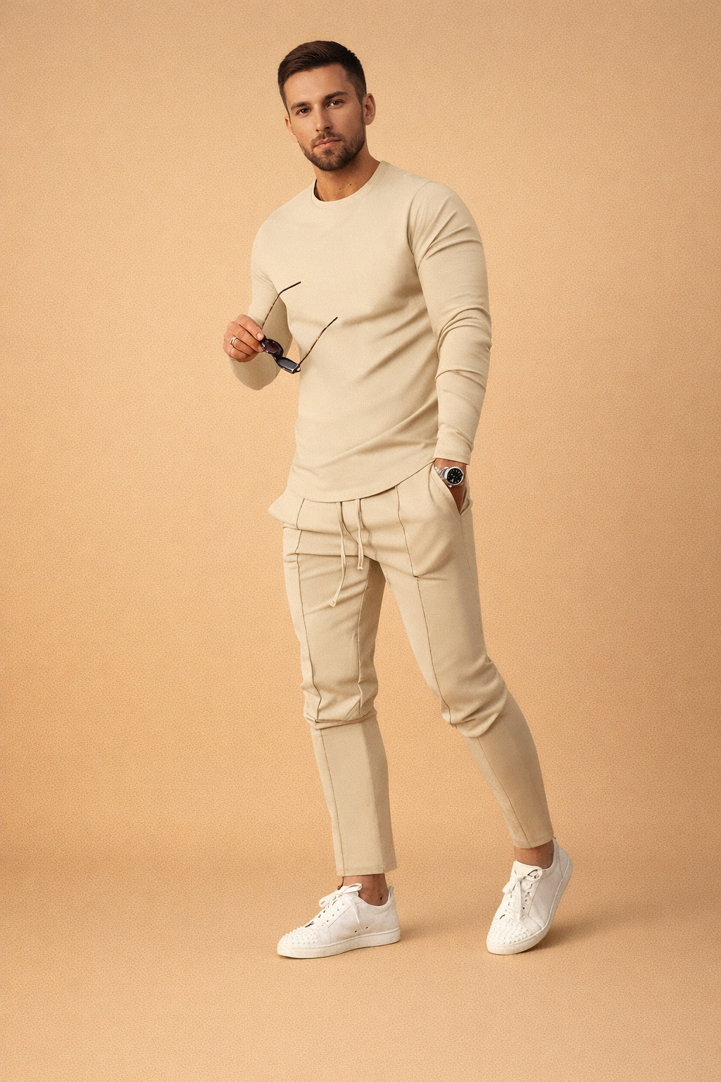 Beige long-sleeve slim-fit knit top paired with matching tailored jogger pants featuring seam piping and drawstring waist, styled with clean white low-top leather sneakers for a modern minimalist casual look