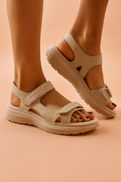 Beige two-strap suede sandals with a cushioned sole and hook-and-loop fastenings, featuring a curved ergonomic silhouette and precise stitching.