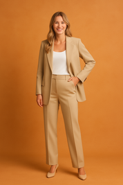 Beige tailored blazer and high-waisted trousers set with a white scoop neck tank top, styled with matching beige heels, against an orange sand-toned background.