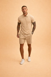 Textured beige short-sleeve zip polo shirt paired with matching tailored linen-blend shorts, featuring a clean minimalist cut, subtle woven fabric texture, tonal stitching, straight hem shorts, and coordinated warm sand color tones, styled with white low-profile sneakers for a refined summer set.