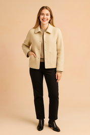 Beige wool short jacket with rounded collar, five matching buttons, and two oversized front patch pockets; smooth felted texture with clean topstitching, styled over a taupe knit and black trousers.
