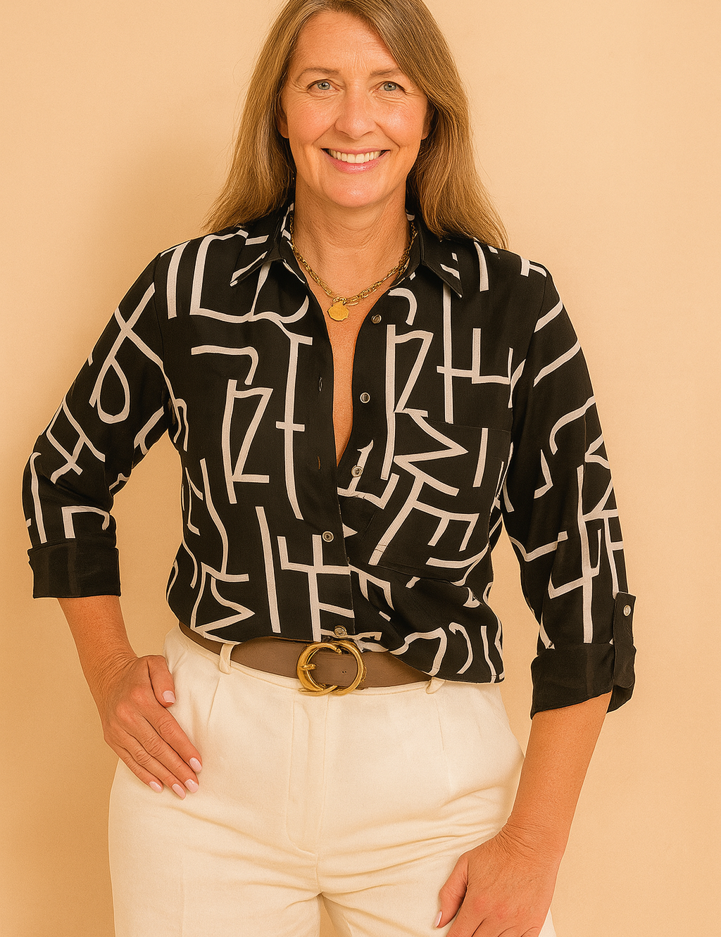 Black button-down shirt with bold abstract white lettering, featuring a sharp collar and rolled sleeves, paired with high-waisted cream trousers and a wide belt with a gold buckle.