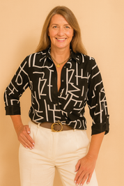 Black button-down shirt with bold abstract white lettering, featuring a sharp collar and rolled sleeves, paired with high-waisted cream trousers and a wide belt with a gold buckle.