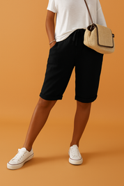 Black cuffed Bermuda shorts with drawstring waist in a lightweight fabric, styled with a white oversized tee and white sneakers for a relaxed casual look.
