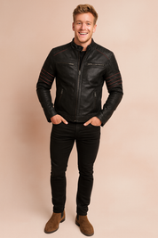 Black biker jacket with red stitched detailing, zippered chest and side pockets, and quilted shoulder panels, styled with slim black jeans and brown suede Chelsea boots for a modern edgy look.