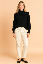 Black cable-knit high-neck sweater paired with cream straight-leg jeans and black low-heeled shoes.