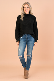 Black cable-knit high-neck sweater paired with distressed blue skinny jeans and taupe ankle boots.
