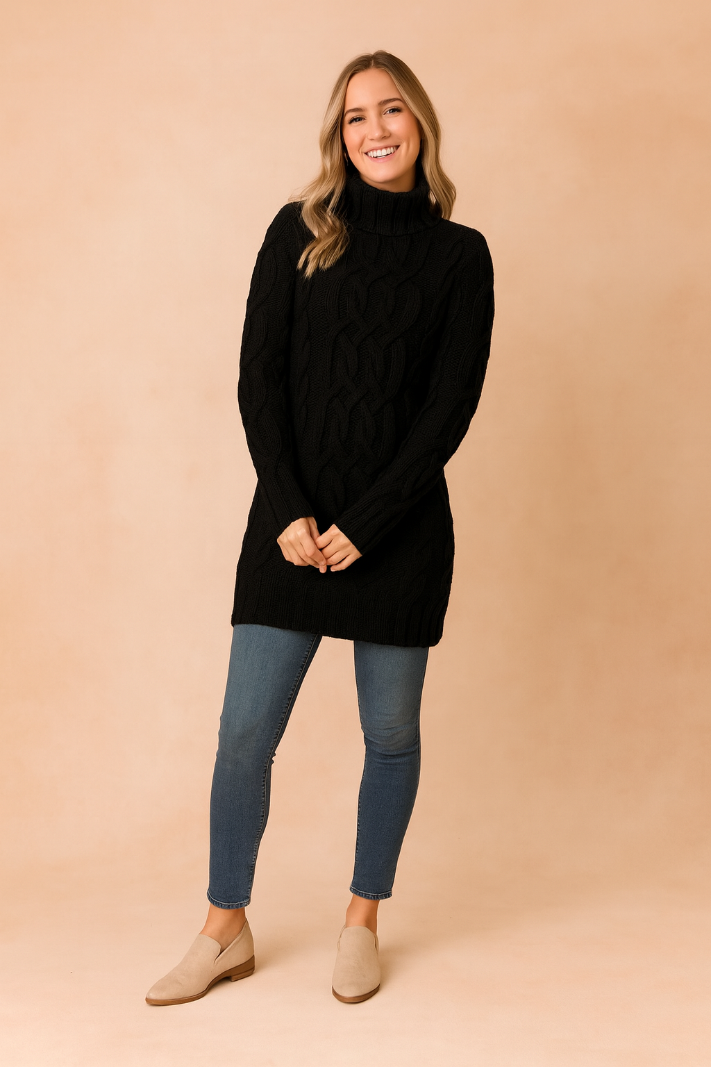 Black cable-knit turtleneck sweater dress paired with medium-wash skinny jeans and beige suede ankle boots.
