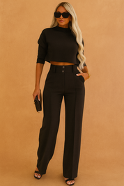 Chic black co-ord set featuring a cropped high-neck long sleeve top and high-waisted wide-leg trousers, styled with black open-toe heels and a small textured clutch for a sleek, modern look.