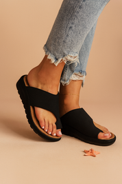 Black cross-strap slide sandals with contoured tan footbeds and textured black outsoles, designed with an open-toe cut and casual ergonomic sole