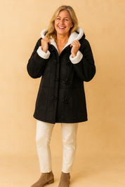 Black duffle coat with white faux shearling lining, paired with cream slim-fit pants and taupe ankle boots.