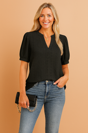 Black short-sleeve eyelet blouse with puffed sleeves, split neckline, and subtle vertical embroidery detailing, styled with blue denim jeans.