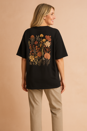 Black oversized T-shirt with floral chest pocket design paired with fitted black pants and black low-top sneakers.
