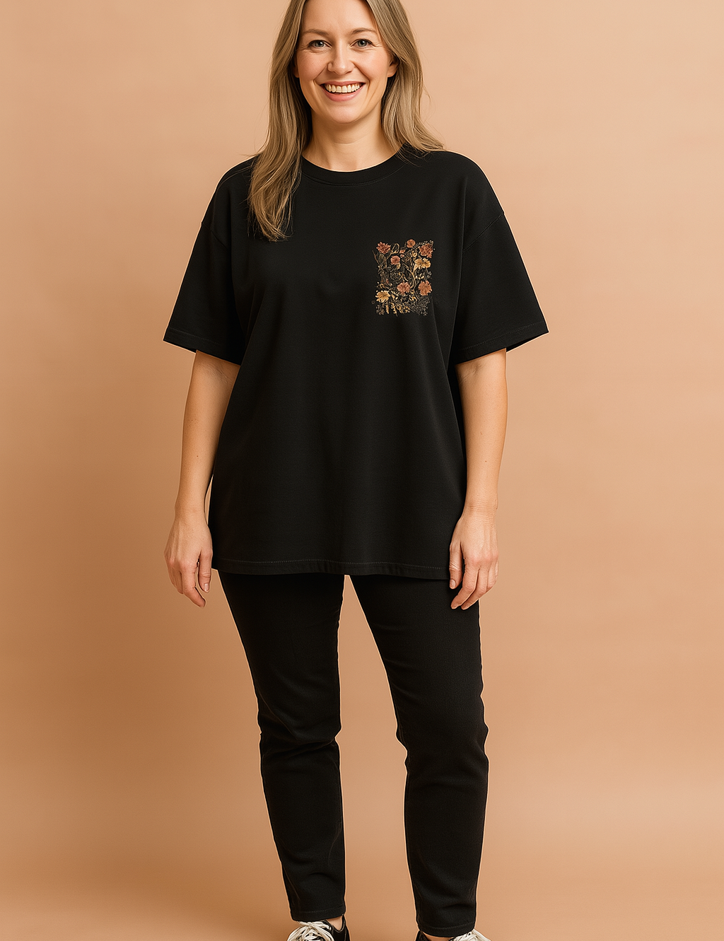Black oversized T-shirt with floral chest pocket design paired with fitted black pants and black low-top sneakers.