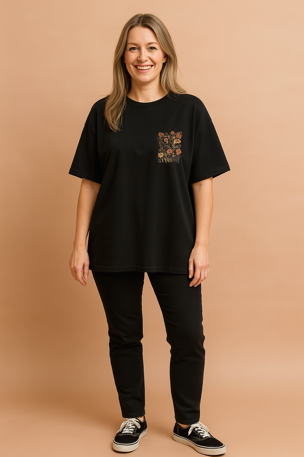 Black oversized T-shirt with floral chest pocket design paired with fitted black pants and black low-top sneakers.