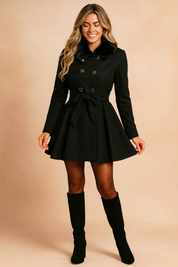 Black double-breasted coat with faux fur collar, gold button detailing, and waist tie belt, styled with a flared hemline, paired with black tights and knee-high suede boots.