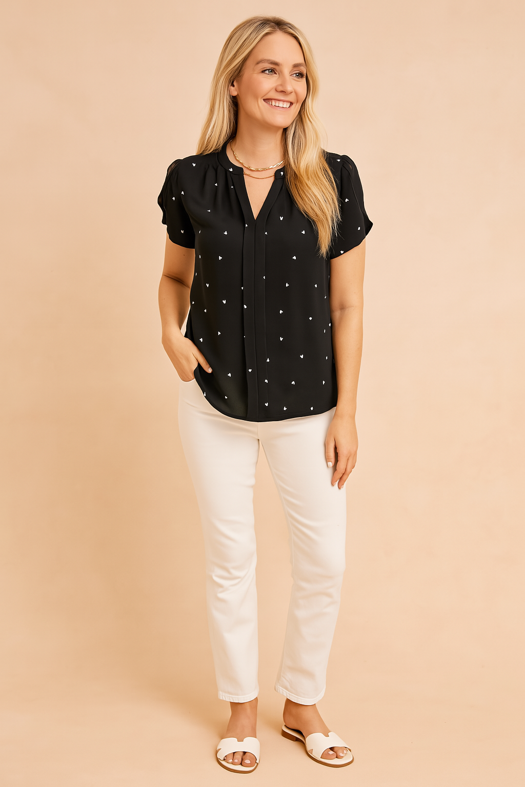 Short-sleeve black blouse with tiny white heart prints, pleated front detailing, and relaxed hem, paired with slim white trousers and white sandals.